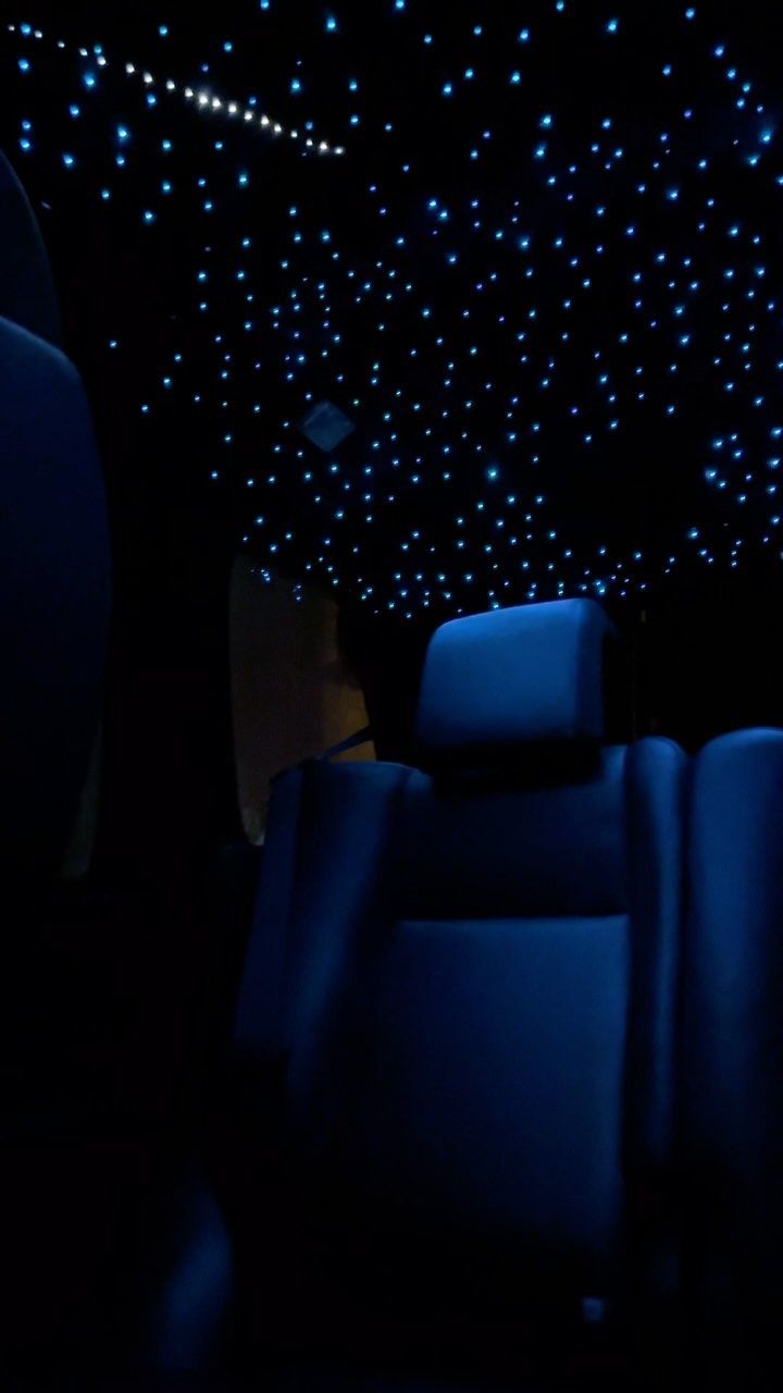 Techo de un coche con cielo estrellado de fibra óptica encendido, sobre los asientos traseros tapizados en azul