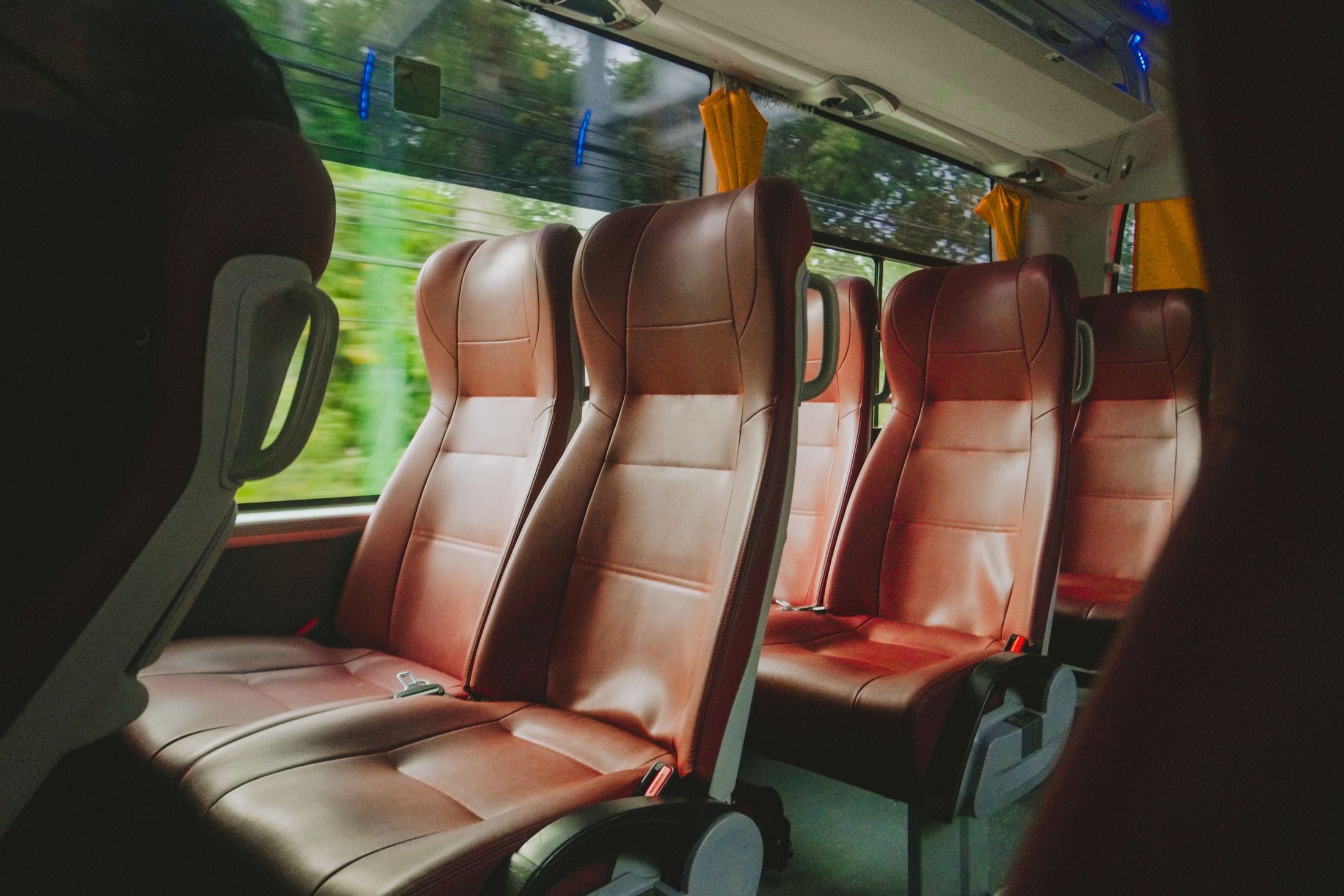Pasillo de una guagua con las filas de asientos vacías, tapizadas en piel granate